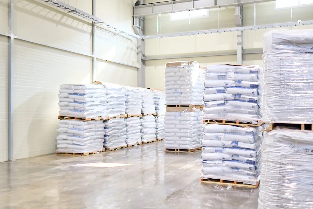 Warehouse interior with rows of sacks stacked on pallets and wrapped in plastic film
