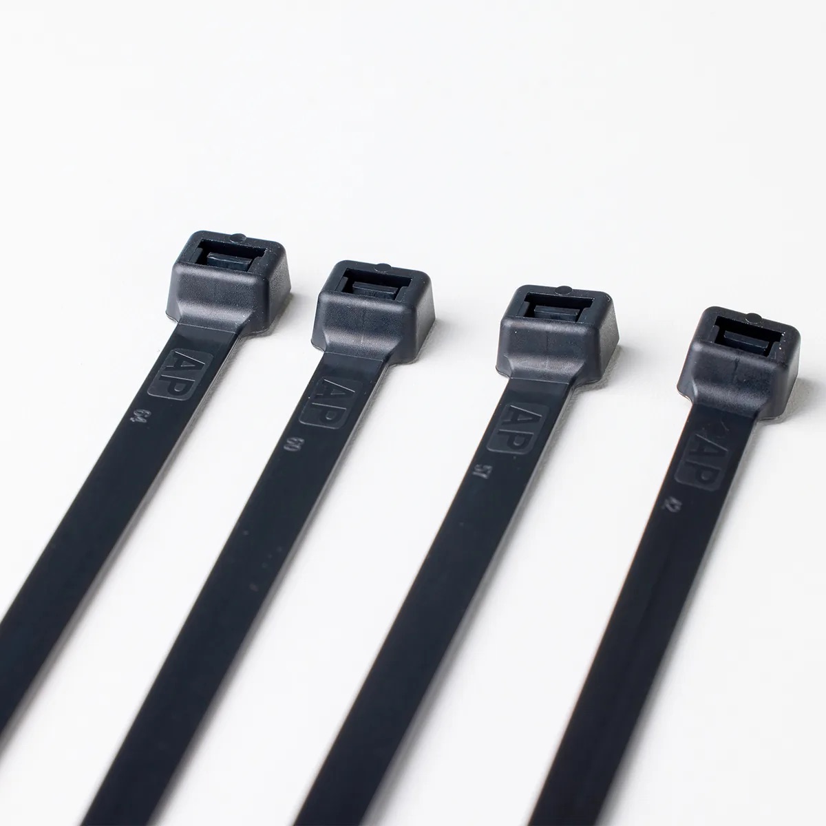 Heads of four black cable ties laid side by side on a white surface, with AP marked on the straps